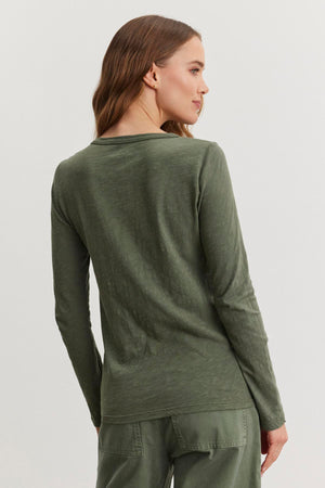 A person with long hair is wearing Velvet by Graham & Spencer's LIZZIE TEE, an olive green cotton slub top, along with pants. The outfit features a subtle crew neckline as they face away.