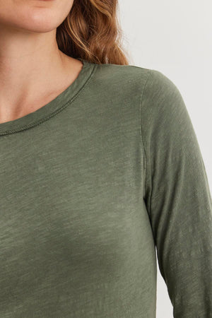 A person is seen wearing the LIZZIE TEE by Velvet by Graham & Spencer, a green cotton slub shirt with a crew neckline, showing only the upper torso and part of the face.