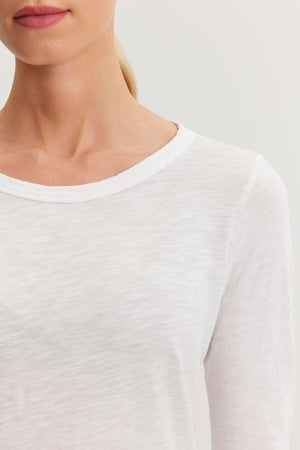 Close-up of the upper body of a person wearing a white, long-sleeve shirt made from textured cotton slub with a classic crew neckline, against a plain background. The shirt is the LIZZIE TEE by Velvet by Graham & Spencer.