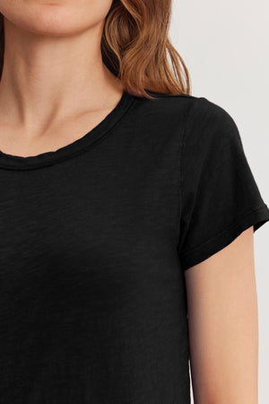 Someone with long hair is wearing the TILLY TEE from Velvet by Graham & Spencer, featuring a plain black crew neck design that embodies an effortless California classic style.