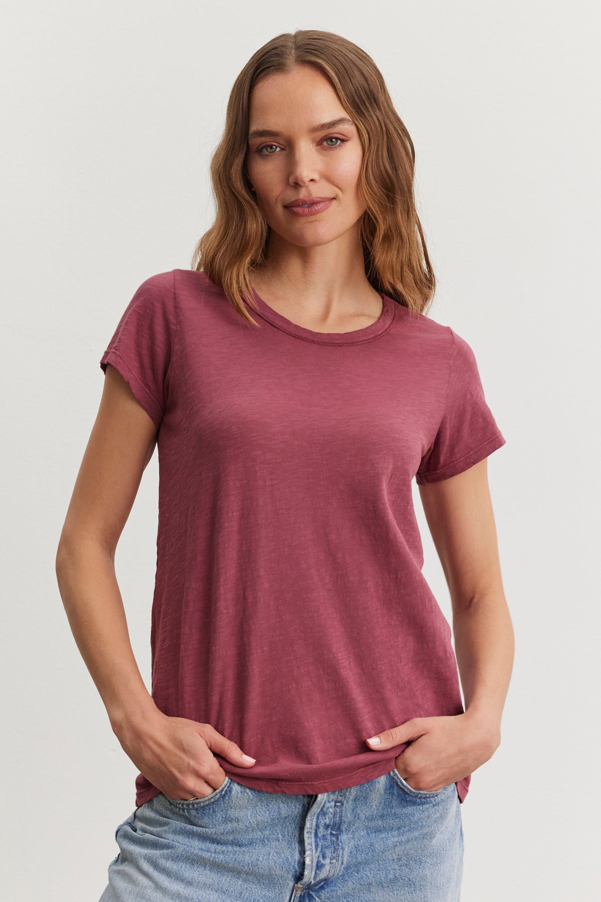   A person in the TILLY TEE by Velvet by Graham & Spencer and blue jeans poses with hands in pockets against a plain background. 