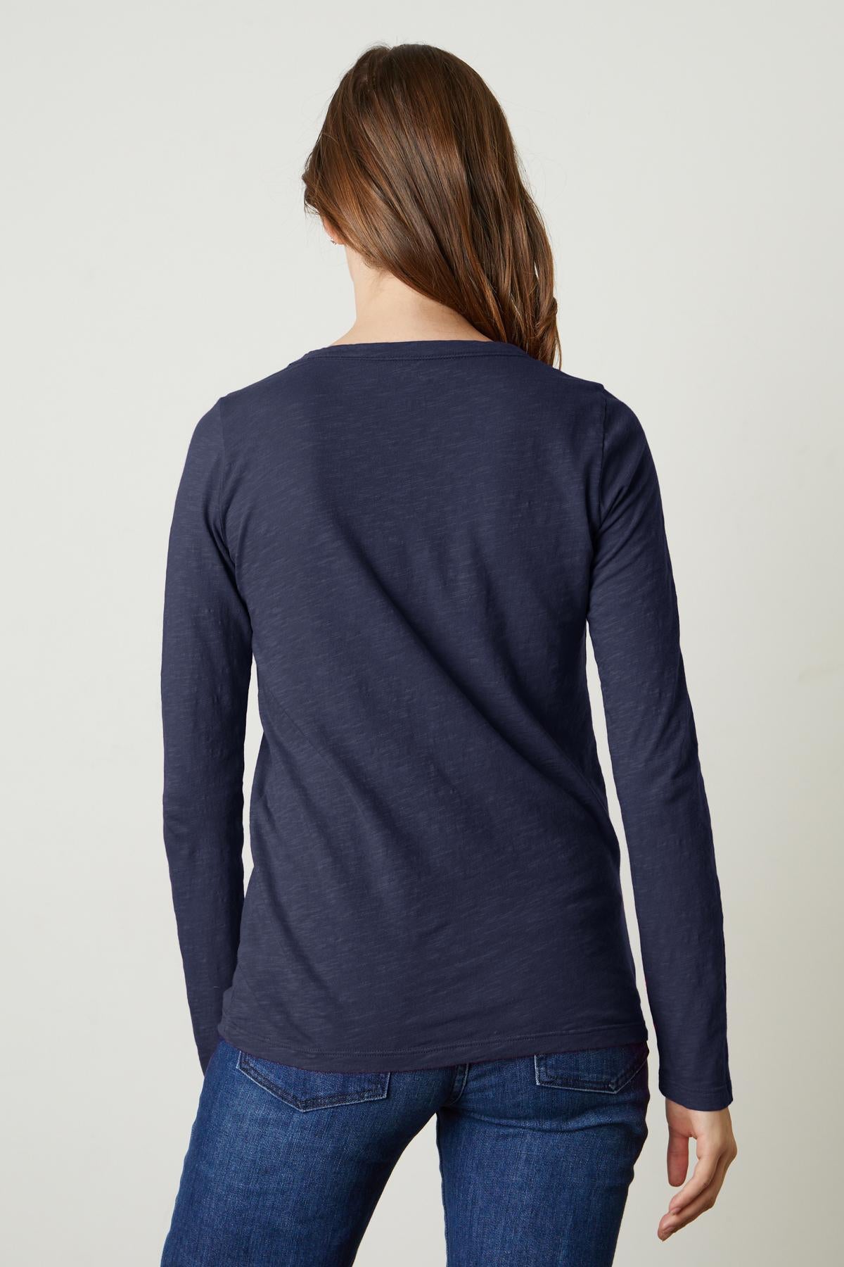   Rear view of a person with long hair wearing a navy blue LIZZIE TEE by Velvet by Graham & Spencer and blue jeans, standing against a plain white background. 