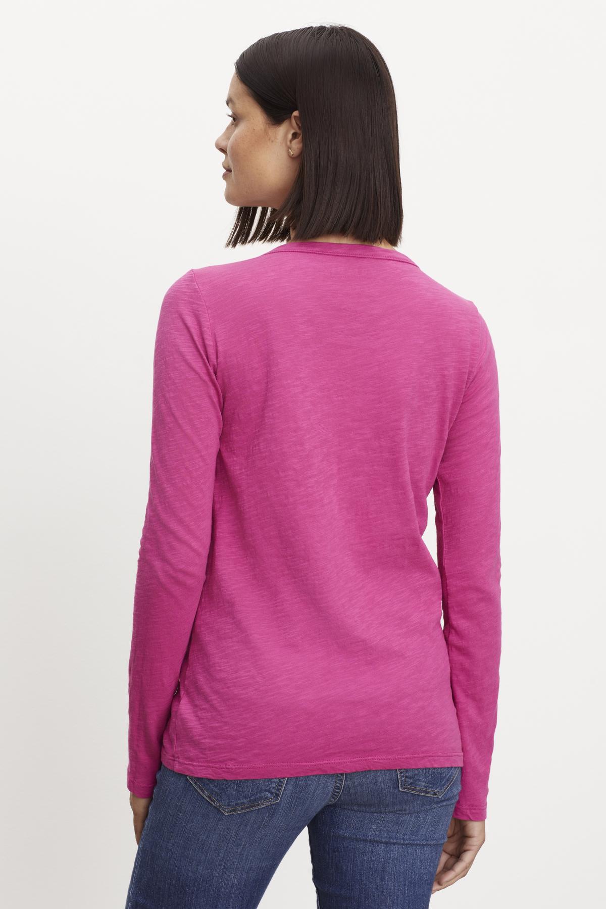   Person standing with back to camera, wearing a bright pink LIZZIE TEE by Velvet by Graham & Spencer and blue jeans. 