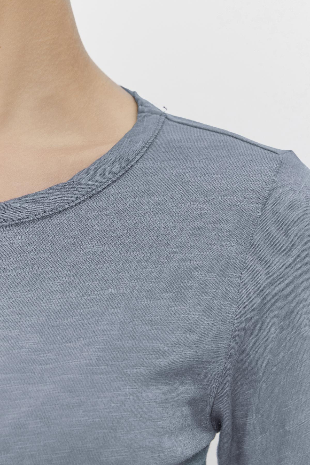   Close-up of a person in the LIZZIE TEE by Velvet by Graham & Spencer, featuring a classic crew neckline and textured cotton slub fabric in light blue with long sleeves. 