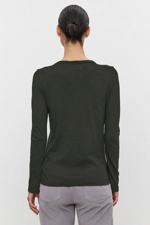 Someone with their hair in a bun is wearing the LIZZIE TEE, a long-sleeved dark green shirt by Velvet by Graham & Spencer, crafted from textured cotton slub. They are also wearing light gray pants, and the view is from behind.