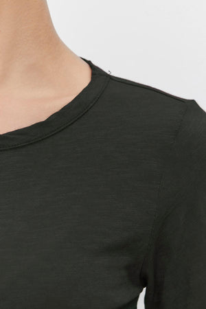 Close-up of a person wearing the LIZZIE TEE by Velvet by Graham & Spencer, featuring a classic crew neckline in dark green. The image highlights the shoulder and part of the upper chest against a neutral background, showcasing the depth and character added by its textured cotton slub fabric to this simple yet stylish piece.