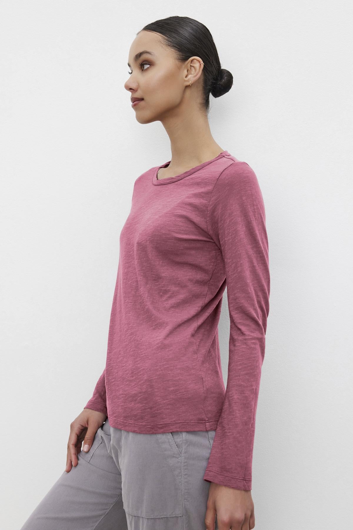   A model stands sideways against a white background wearing the LIZZIE TEE by Velvet by Graham & Spencer, showcasing its maroon cotton slub design with a classic crew neckline and long sleeves. 