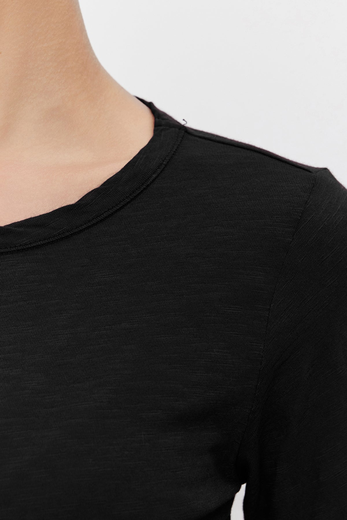   Close-up of a person wearing a black, long-sleeve LIZZIE TEE by Velvet by Graham & Spencer with a classic crew neckline, showing the upper part of the chest and neck against a plain background. 