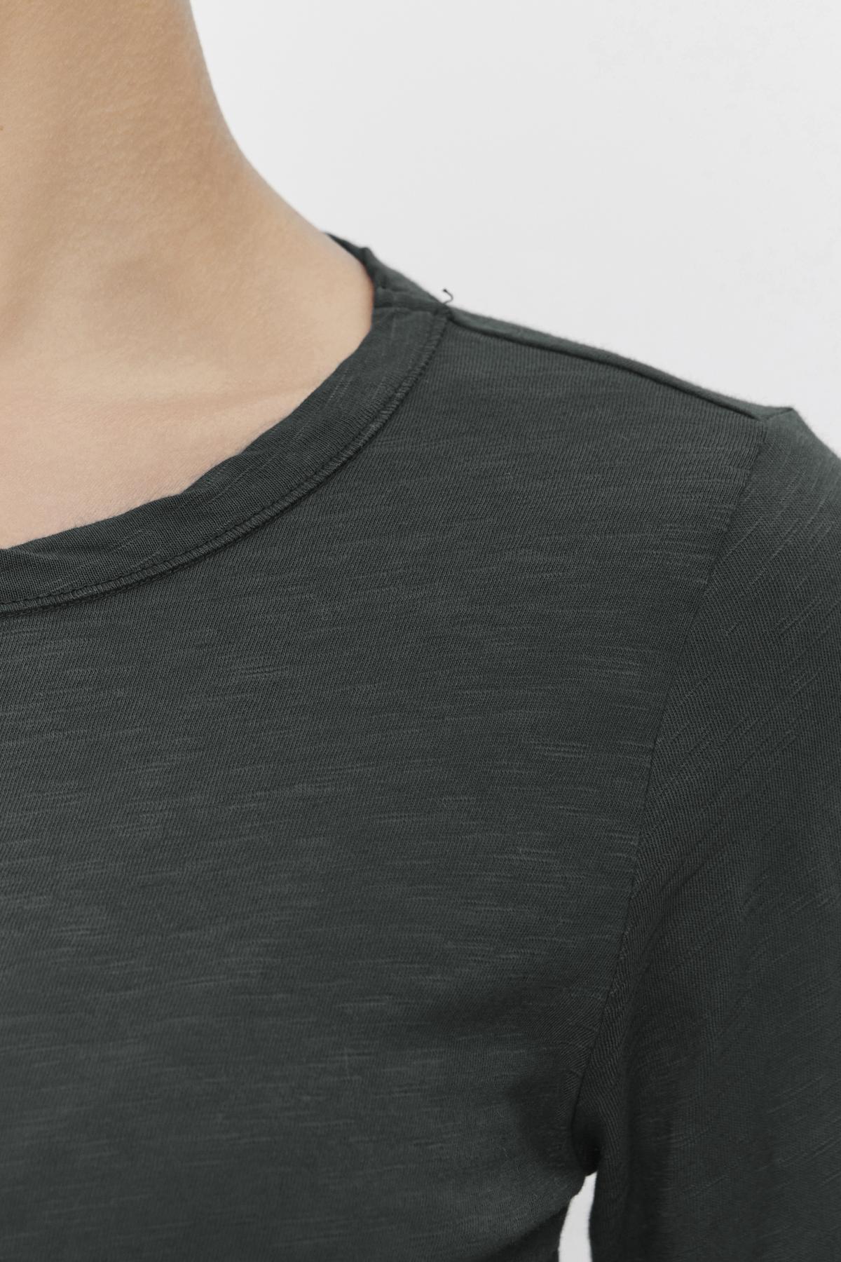 Close-up of a person wearing the Velvet by Graham & Spencer LIZZIE TEE, crafted from soft cotton slub in a dark green shade. The focus is on the shoulder and upper chest area, highlighting the round neckline and long sleeves.-38139494564033