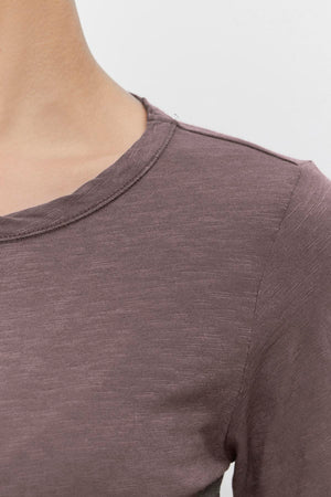 Close-up of a person wearing the LIZZIE TEE, a brown, slightly heathered, long-sleeved shirt from Velvet by Graham & Spencer. The focus is on the upper shoulder and the classic crew neckline of this textured cotton slub tee. The background is plain white.