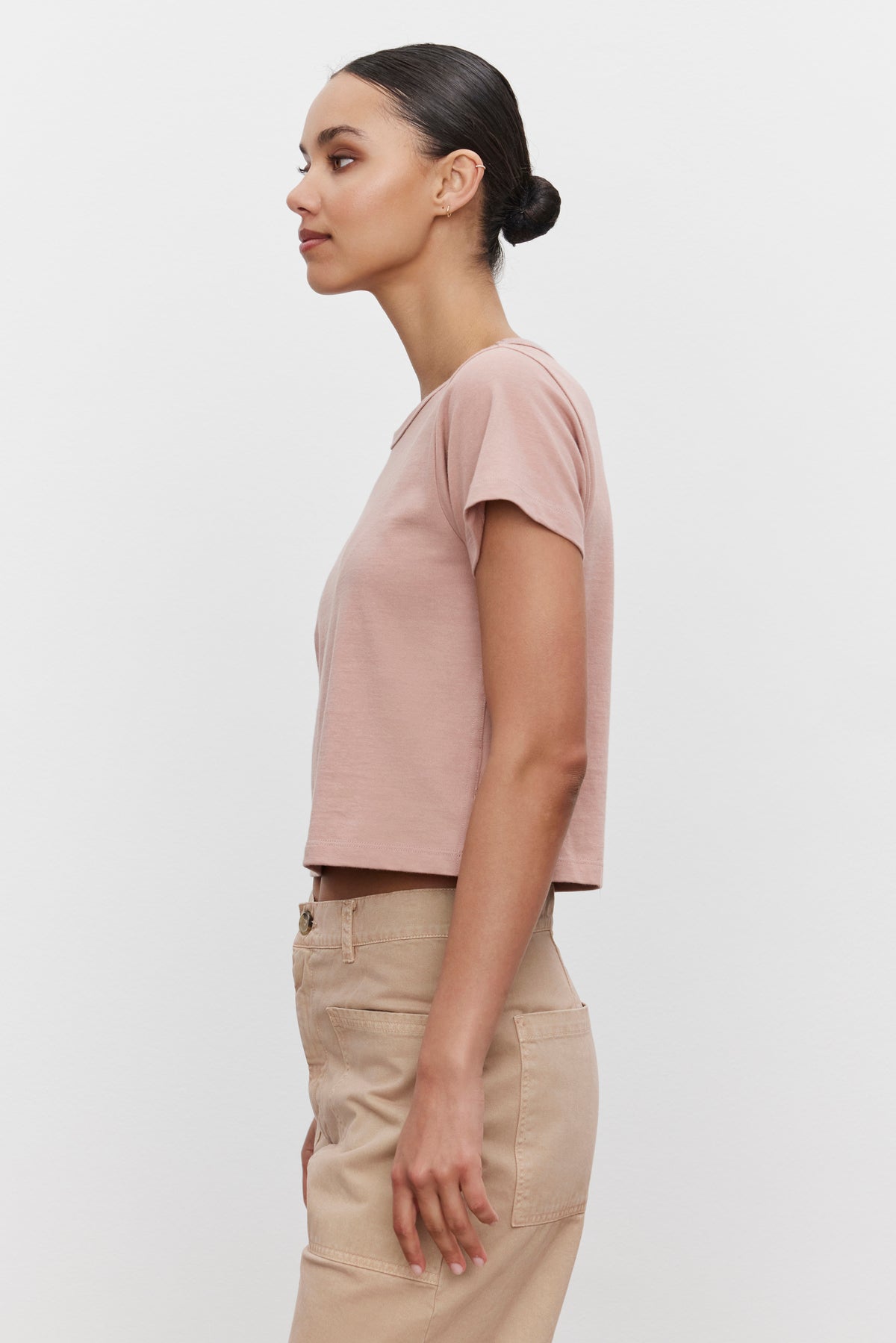 Side view of a person with tied-back hair wearing the TINSLEY TEE in light pink by Velvet by Graham & Spencer, paired with beige pants, exuding a vintage feel.-37629571465409