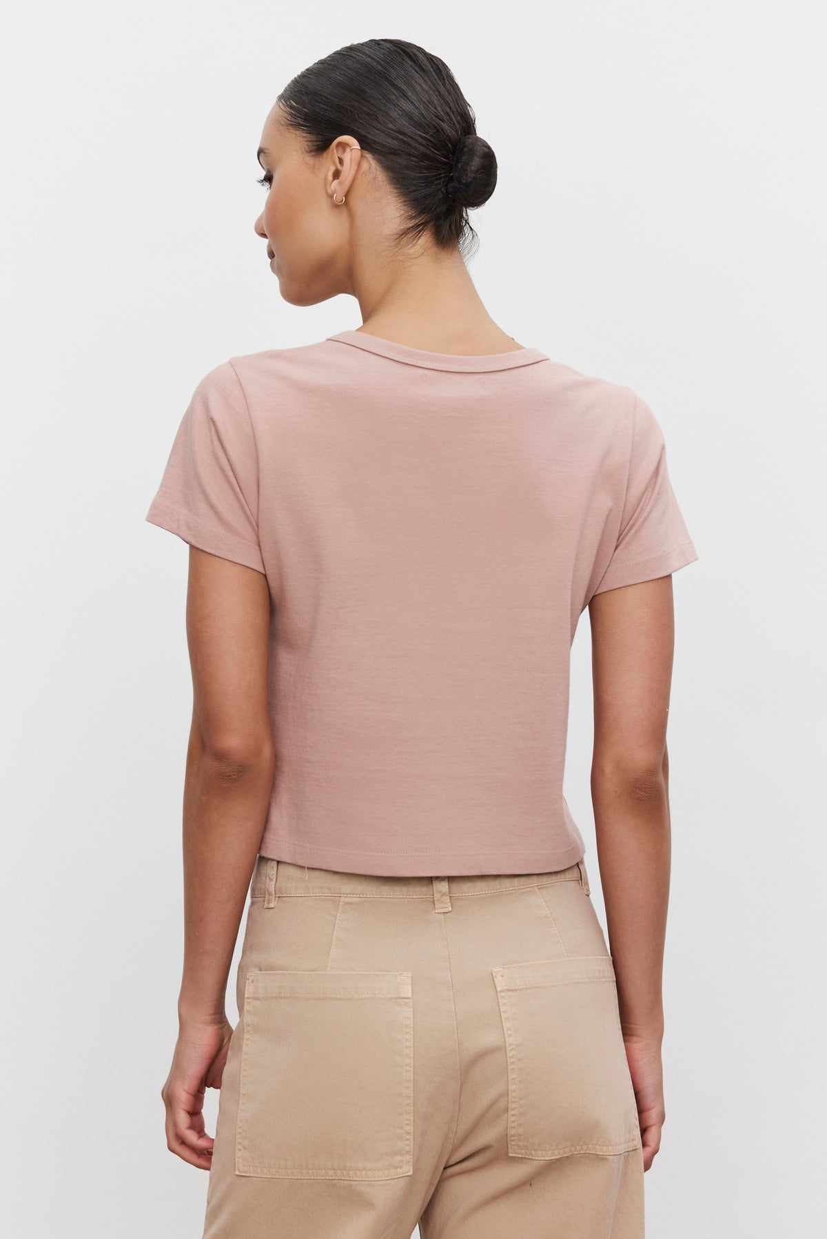   A person with short, slicked-back hair is seen from the back wearing a pink TINSLEY TEE by Velvet by Graham & Spencer and beige pants. 