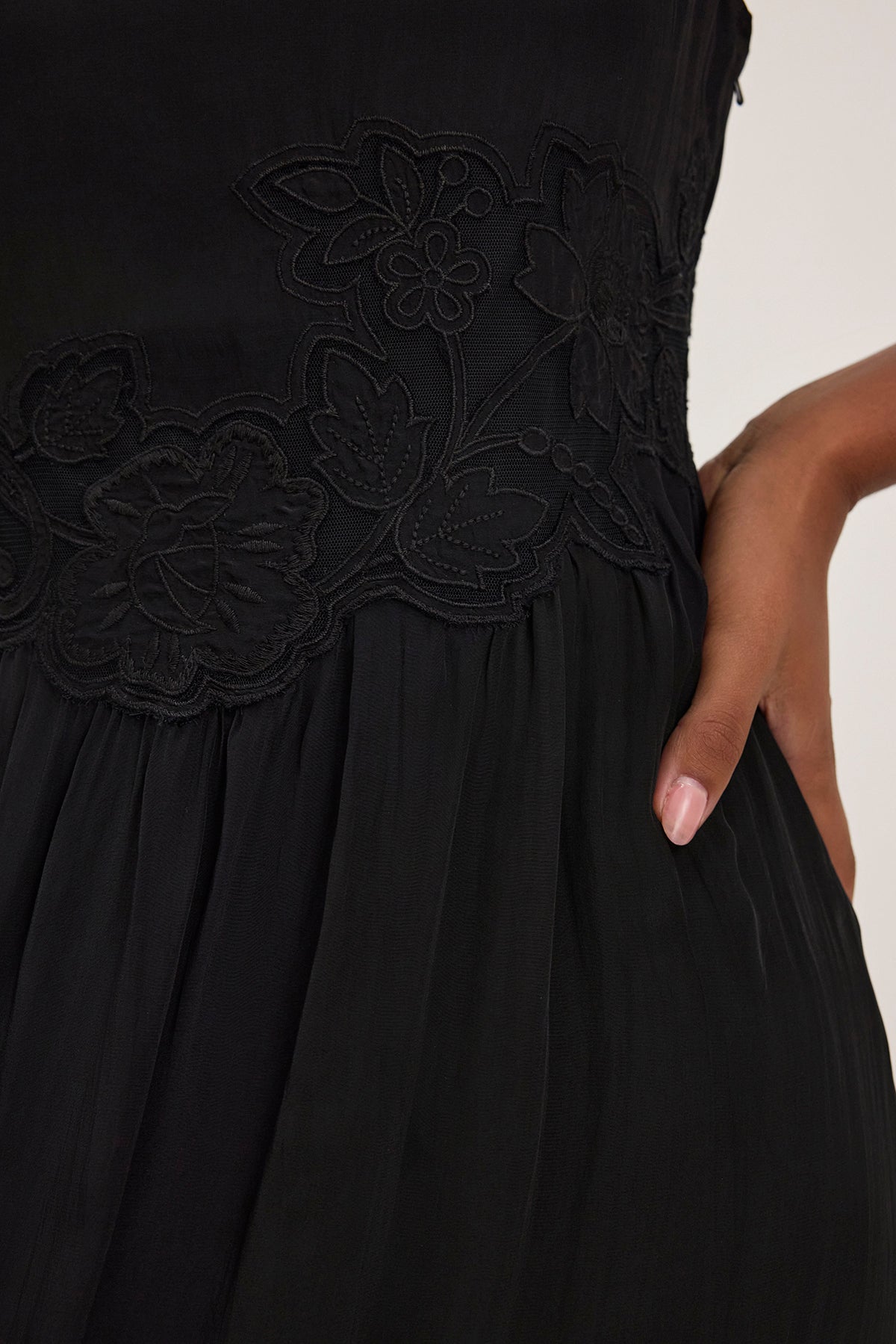   Close-up of a hand holding the waist of the BIANCA DRESS by Velvet by Graham & Spencer, featuring black floral lace embroidery. 