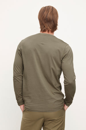 A person with shoulder-length hair wearing an olive green ALVARO HENLEY by Velvet by Graham & Spencer and matching pants is standing with their back facing the camera.