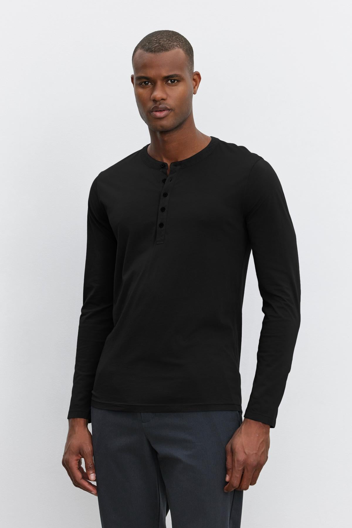 A person is standing against a plain background, wearing a black long-sleeve lightweight ALVARO HENLEY by Velvet by Graham & Spencer and dark jeans.-36273890492609