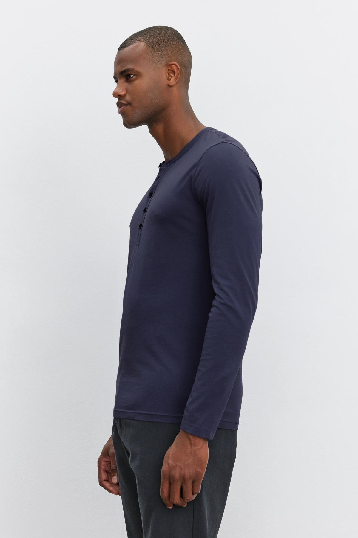 A man is standing in a side view pose, wearing the Velvet by Graham & Spencer ALVARO HENLEY and dark pants against a plain white background.-36273890558145