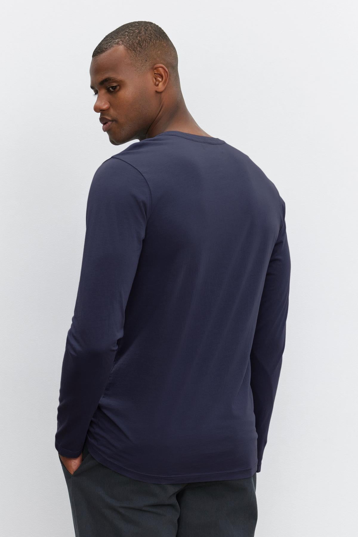 A person wearing a navy blue Velvet by Graham & Spencer ALVARO HENLEY and dark pants stands with their back turned while slightly looking over their shoulder.-36273890590913