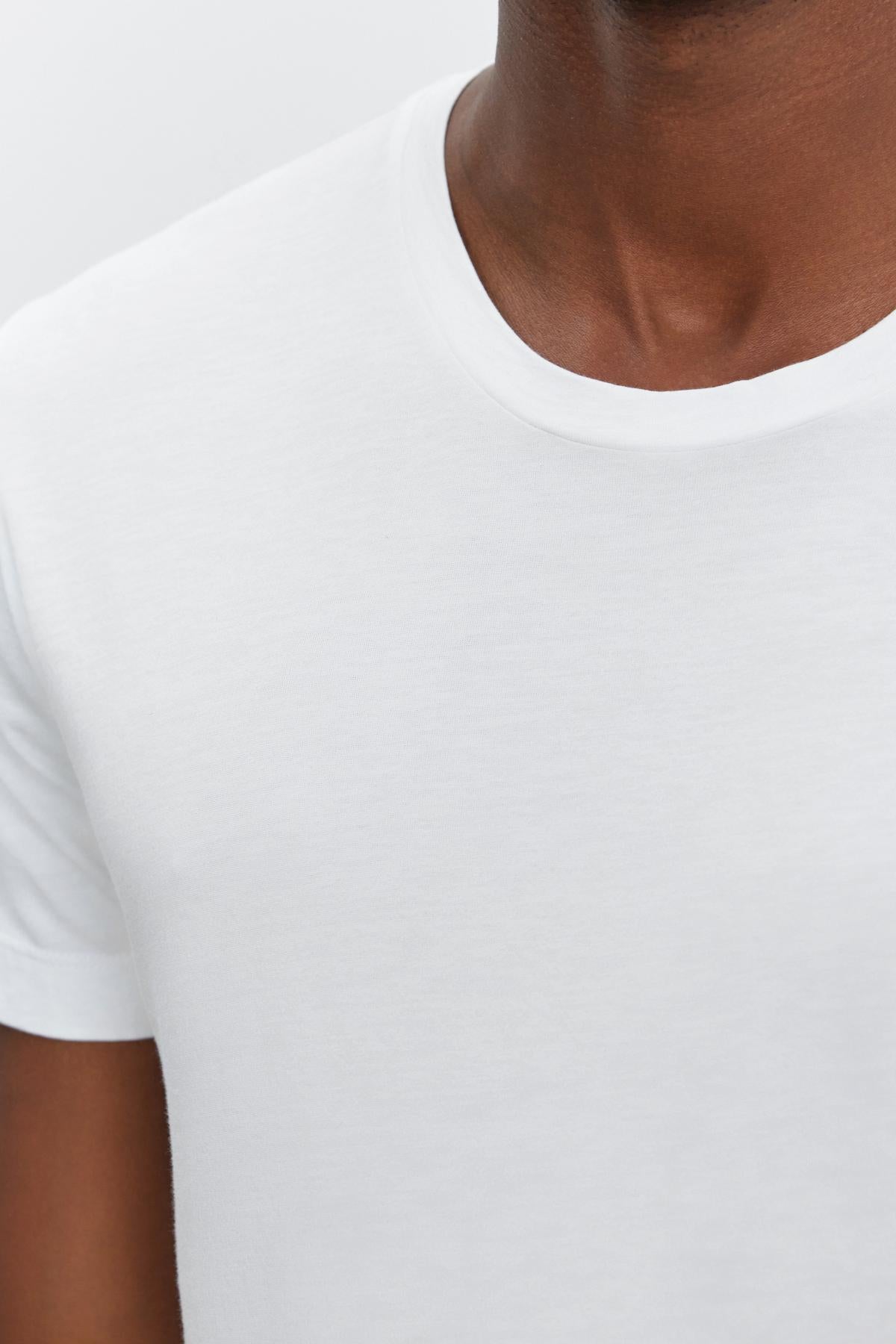   Close-up of a person wearing a plain white HOWARD TEE by Velvet by Graham & Spencer against a neutral background. The image captures the shirt's lightweight cotton knit texture and part of the person's neckline and shoulder, highlighting its perfect fit. 