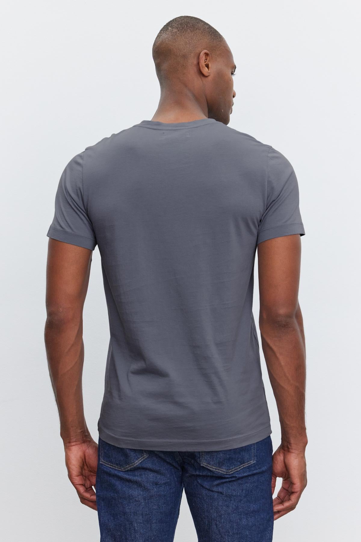   A man is wearing a plain, short-sleeve gray SAMSEN TEE by Velvet by Graham & Spencer and dark blue jeans, facing away from the camera. 