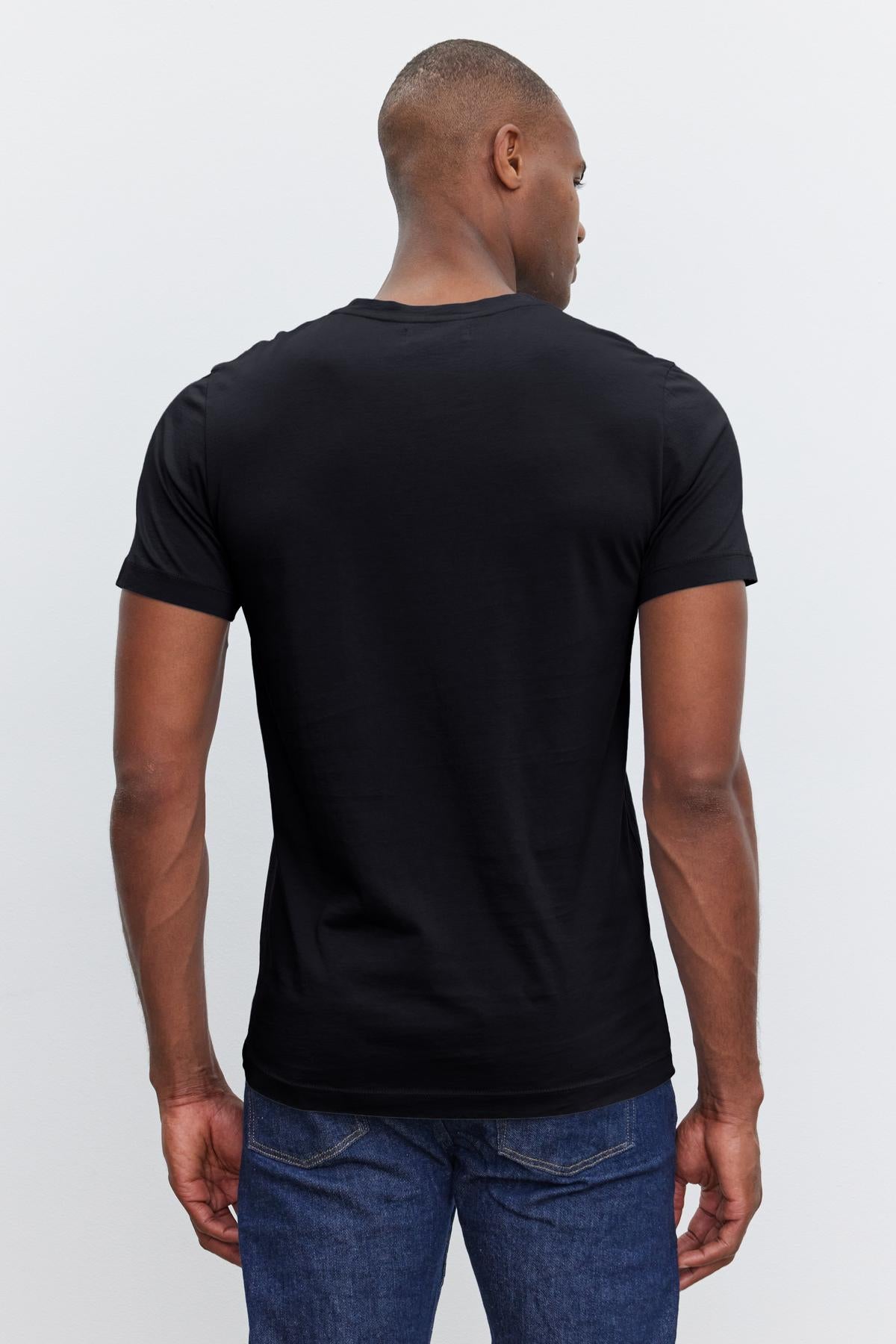   A person wearing a plain black SAMSEN TEE by Velvet by Graham & Spencer and blue jeans, showcasing a flawless fit, is shown from the back. 