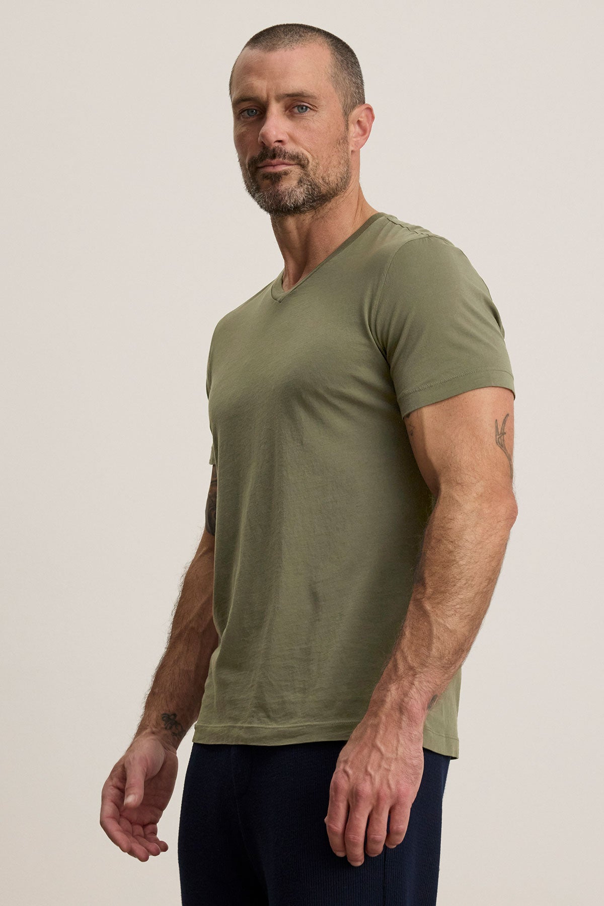   A person in a SAMSEN TEE by Velvet by Graham & Spencer, featuring a green v-neckline and soft Pima jersey, pairs it with dark pants against a plain background, effortlessly showcasing an essential layering piece for any wardrobe. 