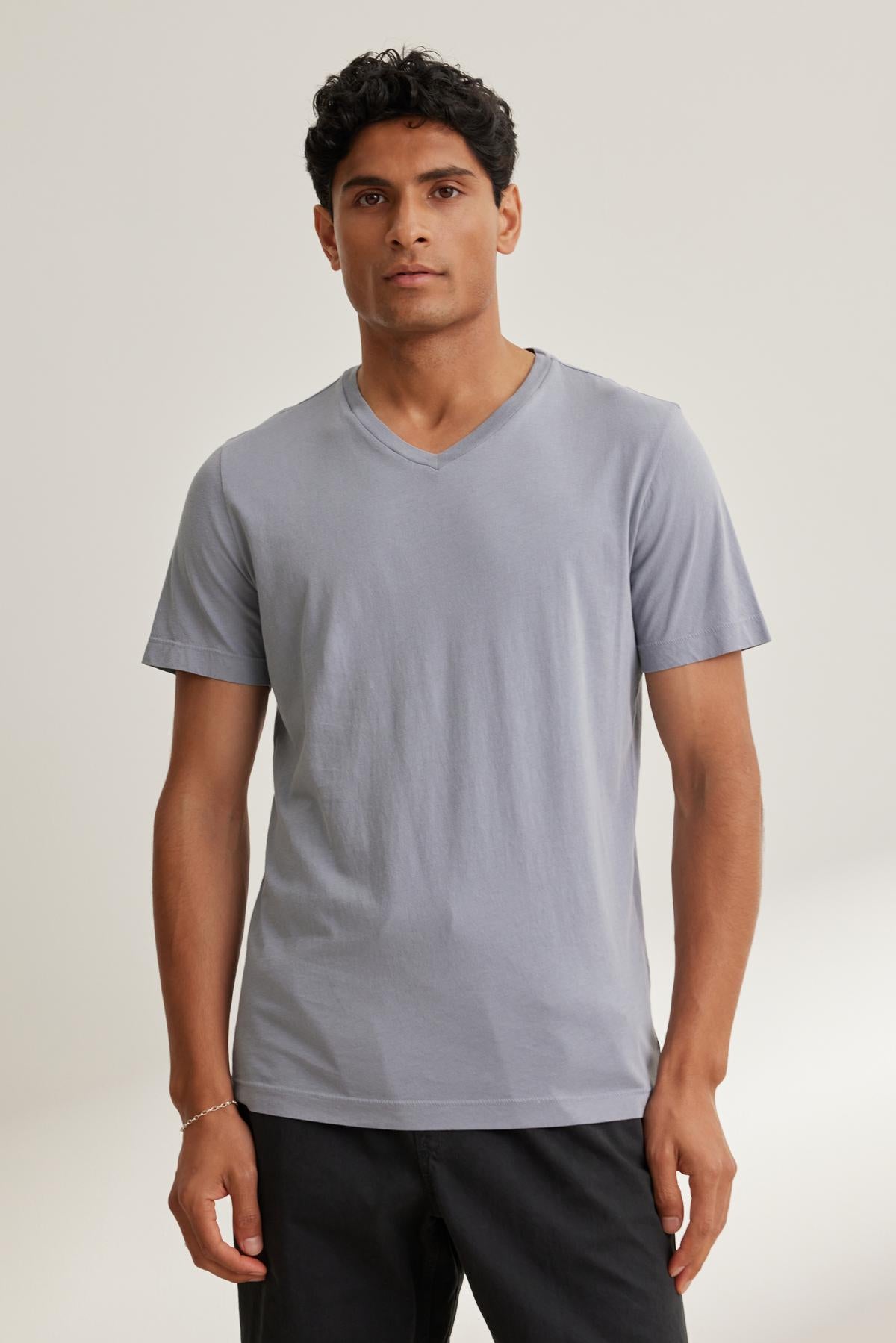   A person wearing a light gray SAMSEN TEE by Velvet by Graham & Spencer paired with black pants stands against a simple background. 