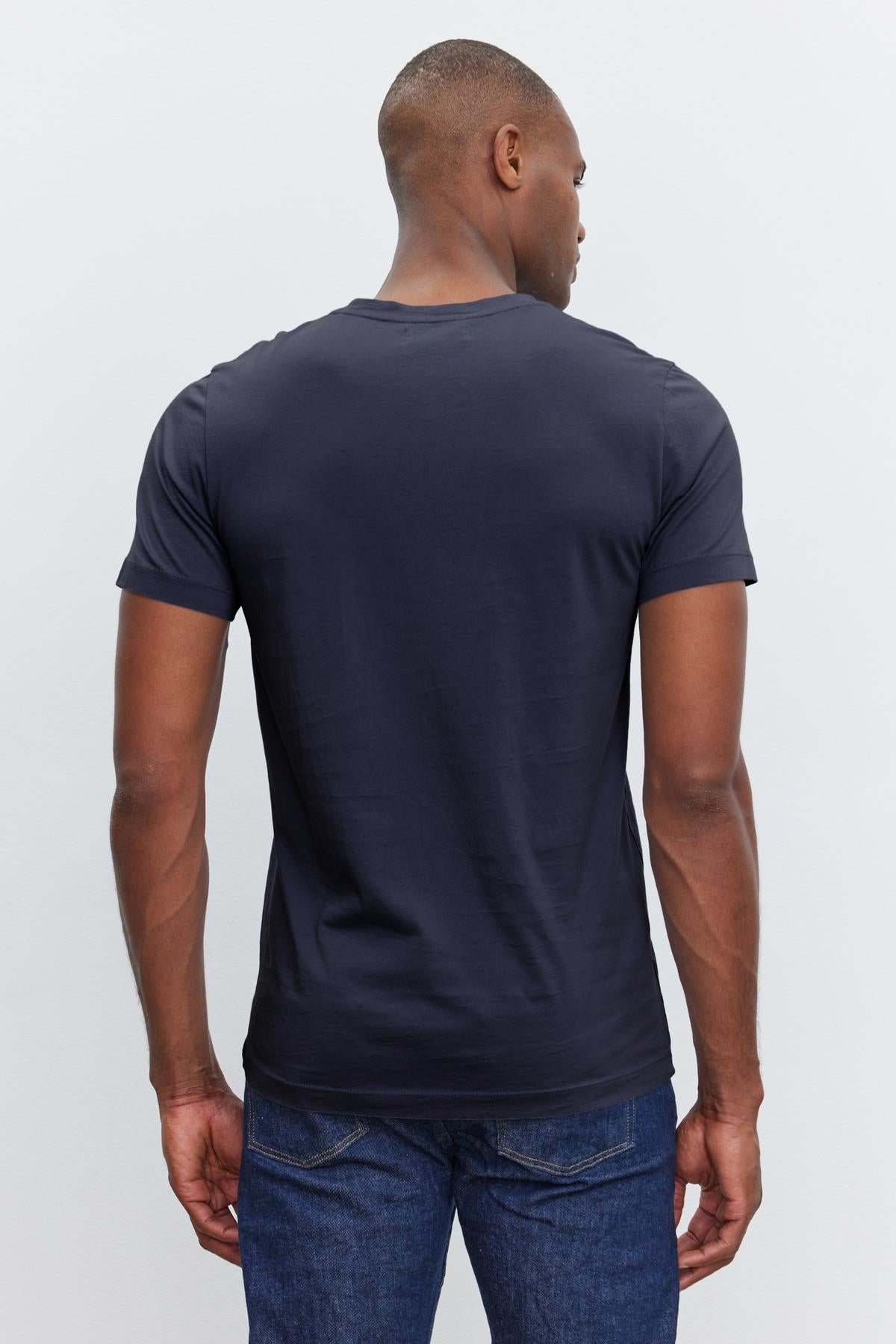   Man wearing a dark navy short-sleeve SAMSEN TEE by Velvet by Graham & Spencer with a whisper knit for a flawless fit and blue jeans, facing away from the camera, with his head turned slightly to the left. 