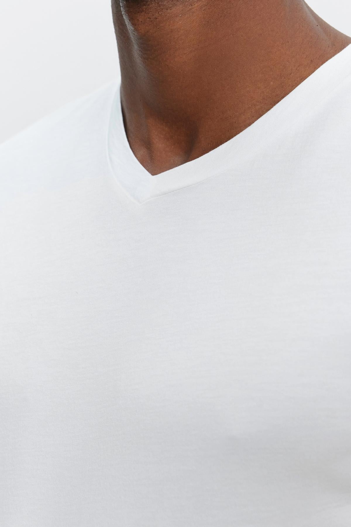   Close-up view of a person wearing a plain white SAMSEN TEE by Velvet by Graham & Spencer with a flawless fit against a light background. Only the lower part of the face and neck are visible. 