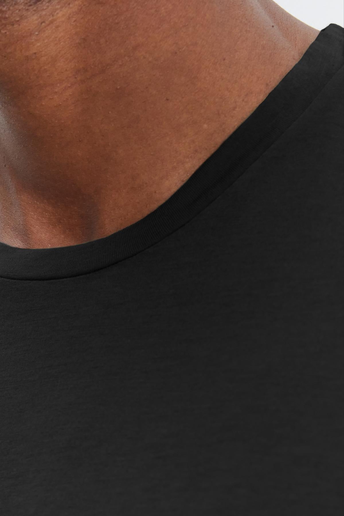   Close-up of a person's neck and upper chest wearing a black SKEETER TEE by Velvet by Graham & Spencer, a versatile wardrobe addition. 