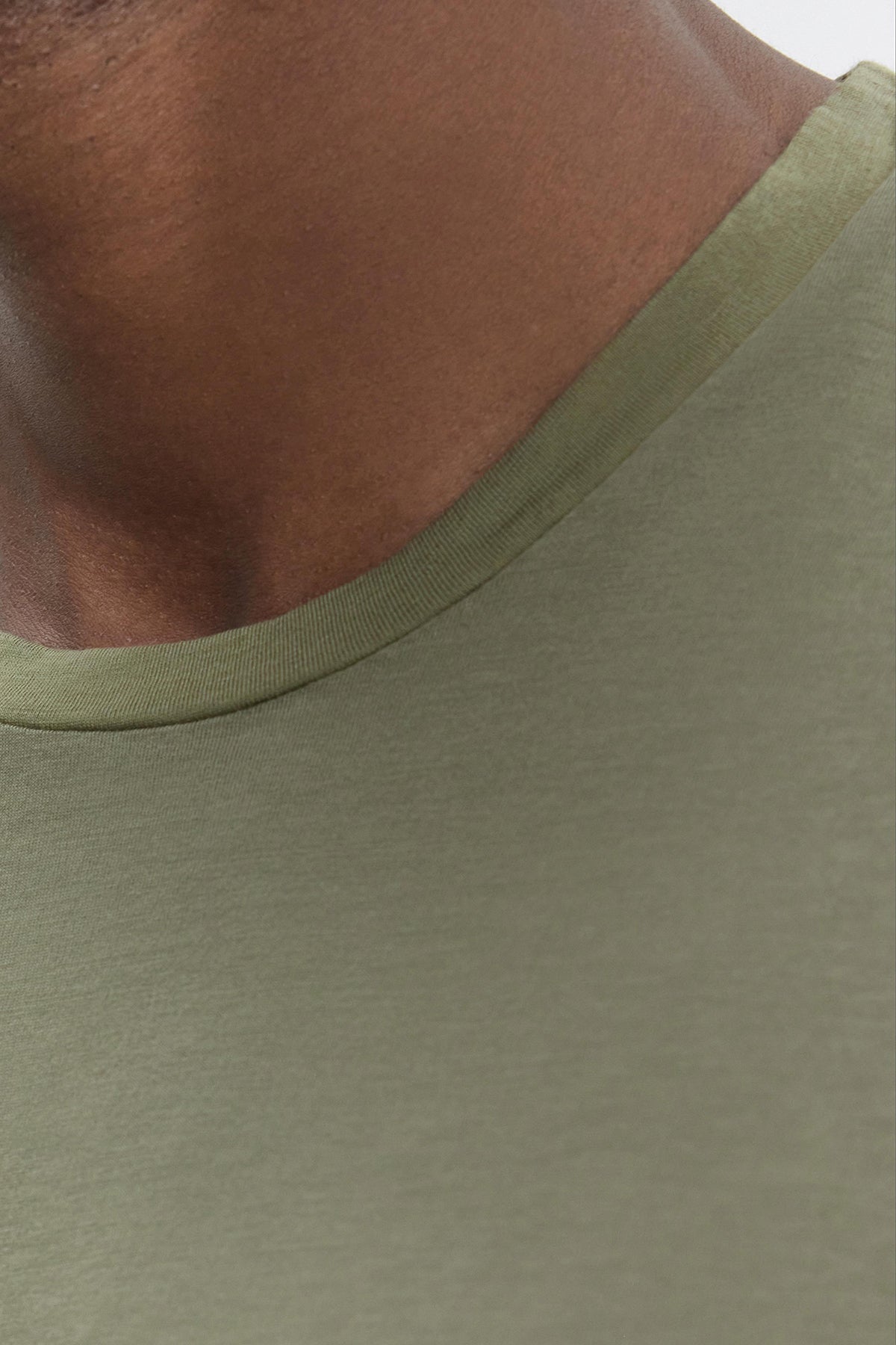   Close-up of a person wearing a green SKEETER TEE from Velvet by Graham & Spencer, made from soft Pima cotton, showcasing their neck and shoulder area with its classic crew neckline. 