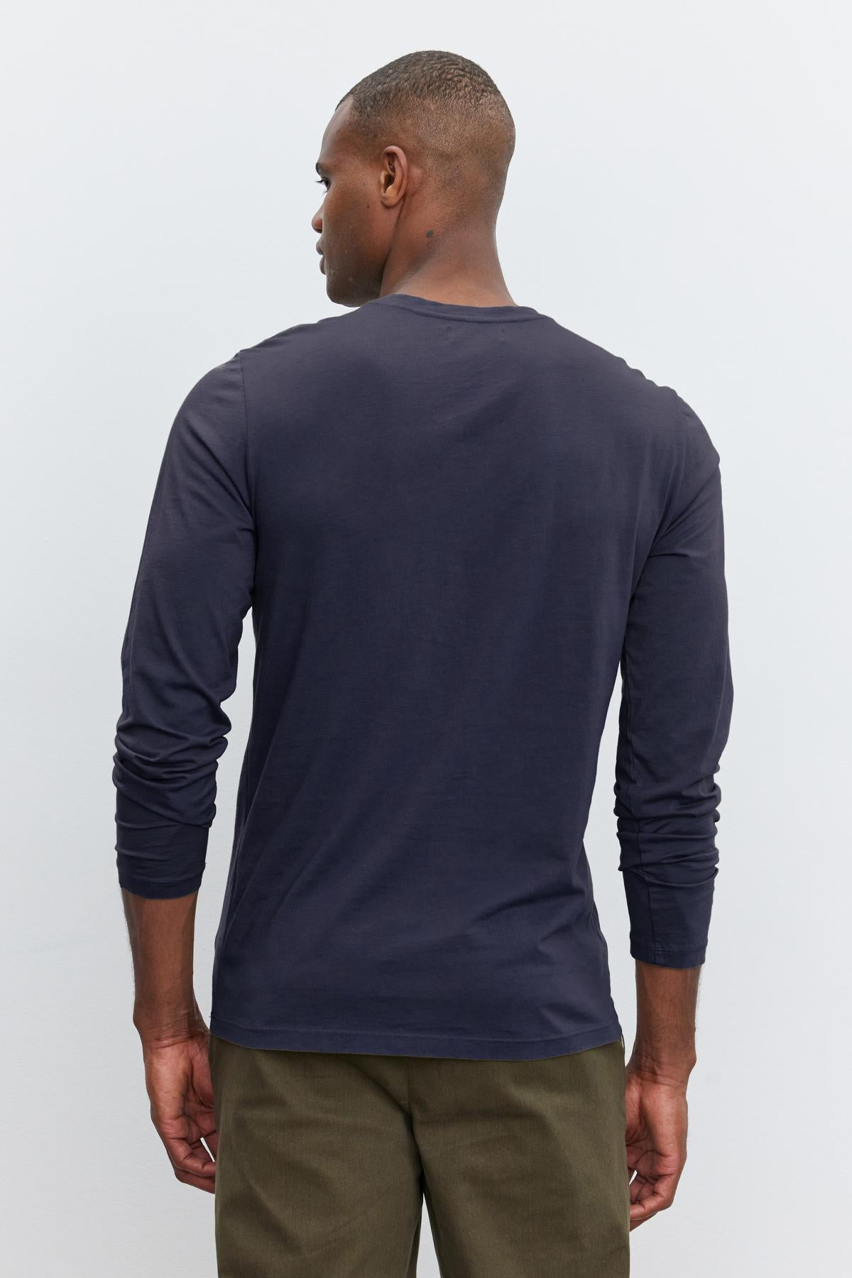 A person with short hair is facing away from the camera, donning a Velvet by Graham & Spencer SKEETER TEE and olive green pants against a plain white background.-36342439379137