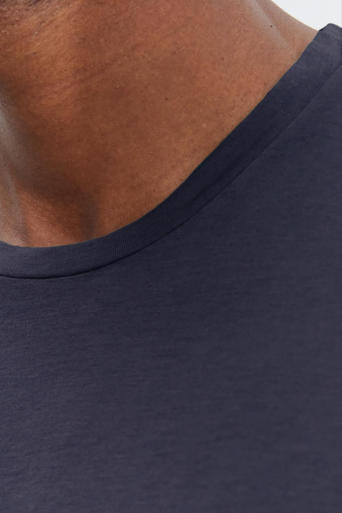   Close-up of an individual wearing a dark blue crew-neck SKEETER TEE from Velvet by Graham & Spencer, focusing on the whisper cotton knit neckline and part of the shoulder. 