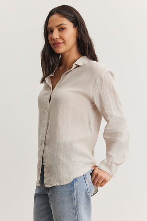 A woman wearing a Velvet by Graham & Spencer Willow Linen Button-Up Shirt and blue jeans, standing with one hand on her hip and looking relaxed.