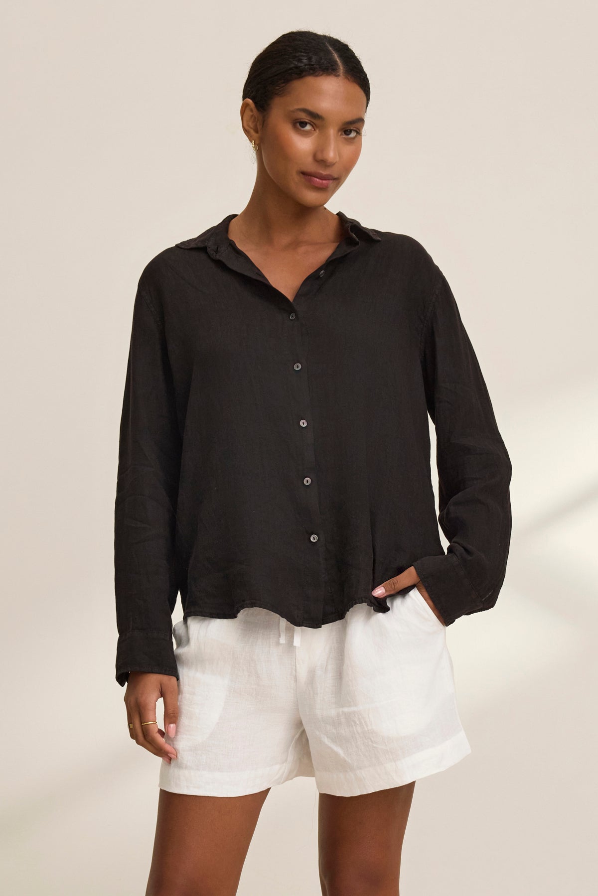   Wearing a black long-sleeve shirt and Velvet by Graham & Spencer's AMBER LINEN SHORT, a person stands with one hand in pocket against a plain background. 