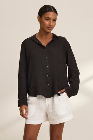 Wearing a black long-sleeve shirt and Velvet by Graham & Spencer's AMBER LINEN SHORT, a person stands with one hand in pocket against a plain background.