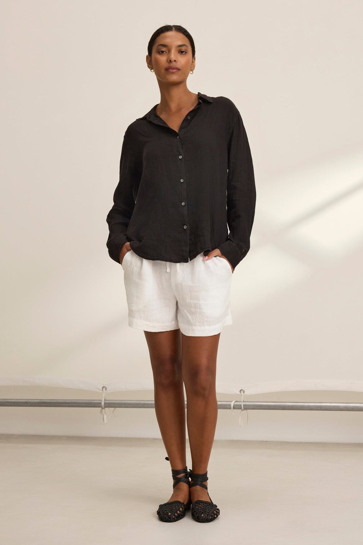   A person in a black long-sleeve shirt, AMBER LINEN SHORT by Velvet by Graham & Spencer, and black sandals stands against a light background. 