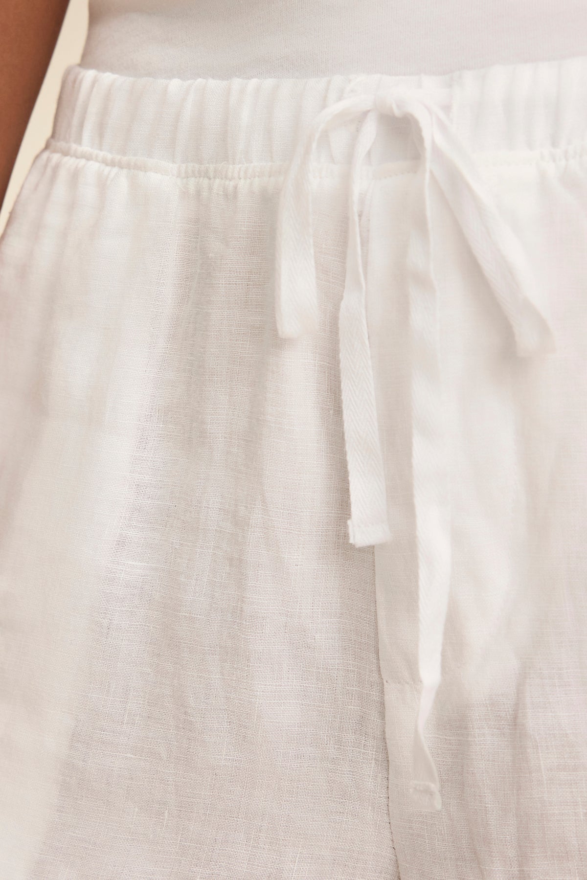   Close-up of someone wearing Velvet by Graham & Spencer's AMBER LINEN SHORT, featuring a drawstring waist and breathable fabric, paired with a white top for a relaxed fit perfect for warm weather. 