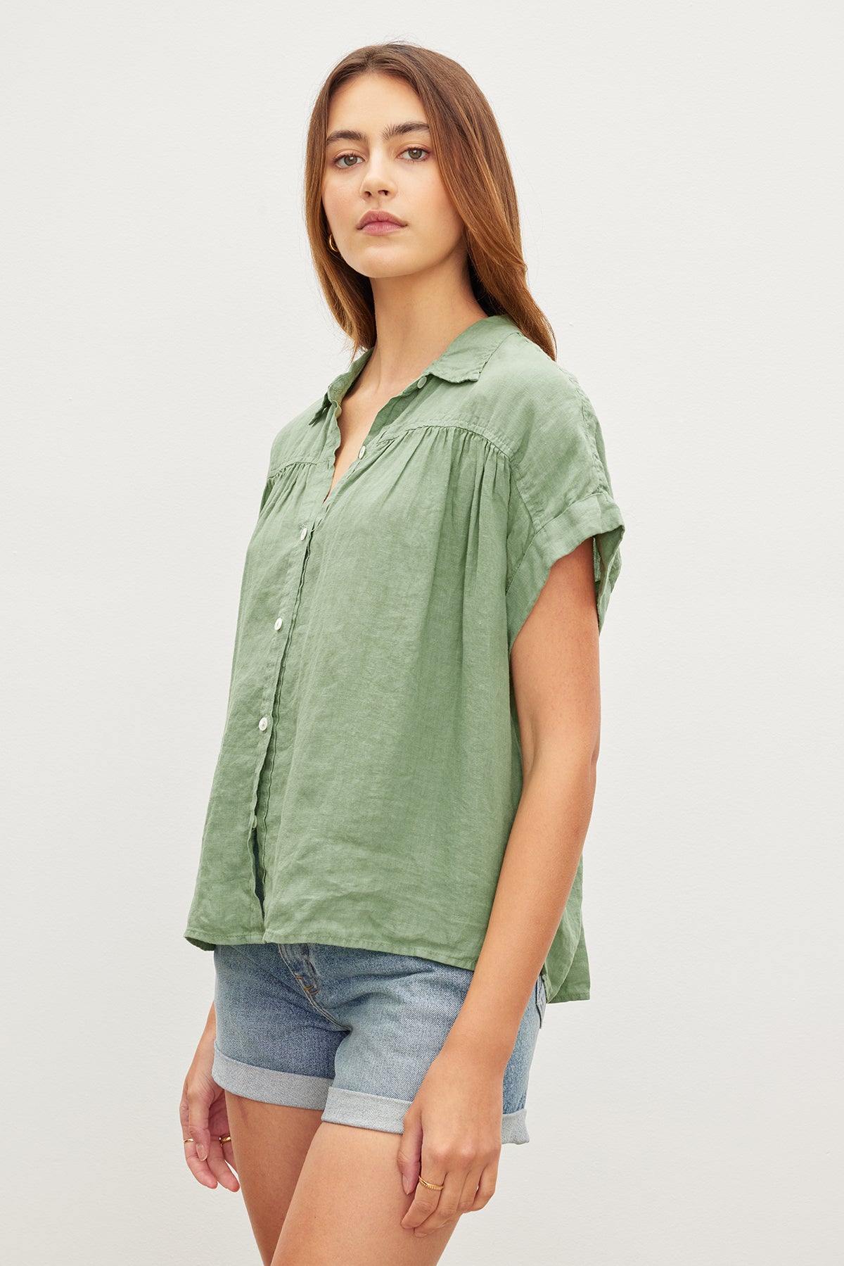 A person in the ARIA LINEN TOP, a versatile piece by Velvet by Graham & Spencer, and denim shorts stands against a plain background.-35955415056577