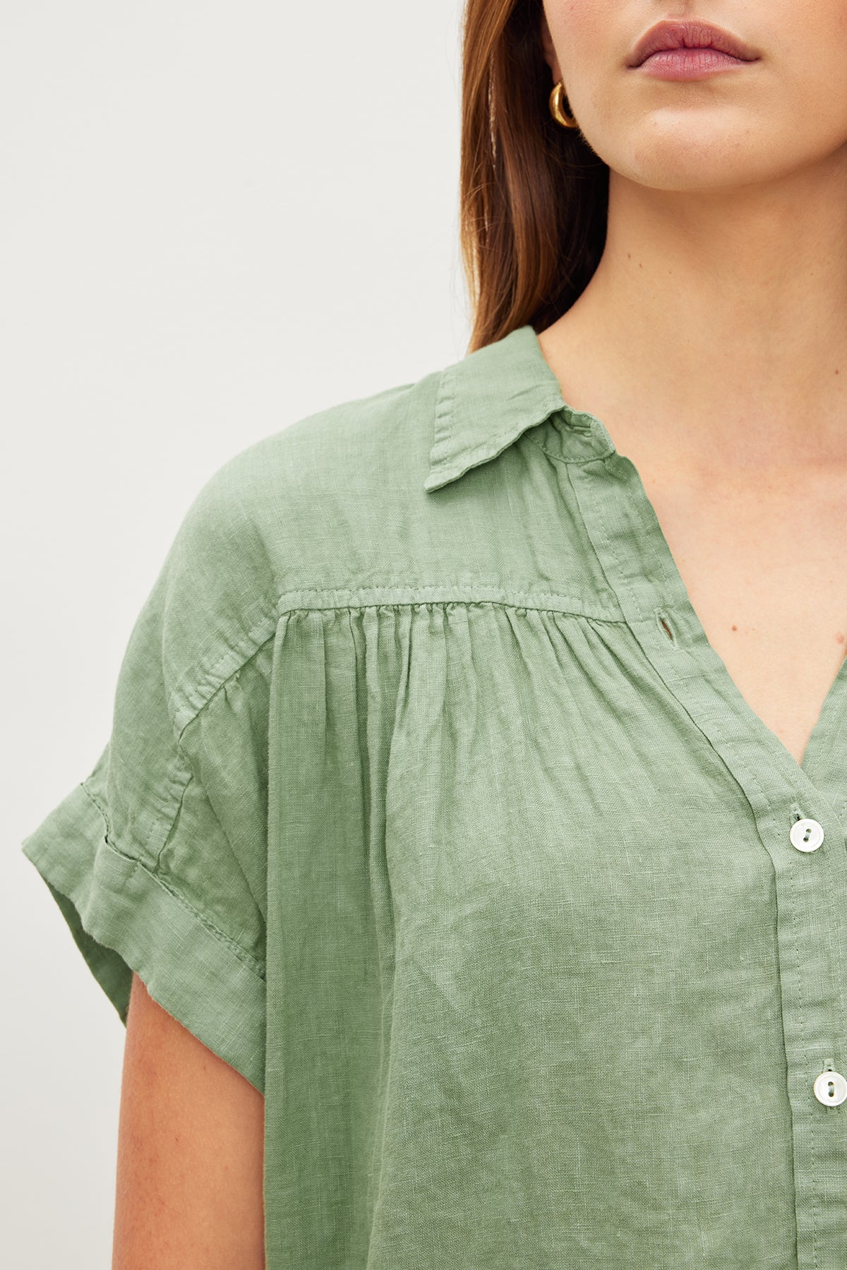   A person wearing the ARIA LINEN TOP, a versatile green blouse by Velvet by Graham & Spencer, featuring button details and a classic collar, stands against a plain background. 