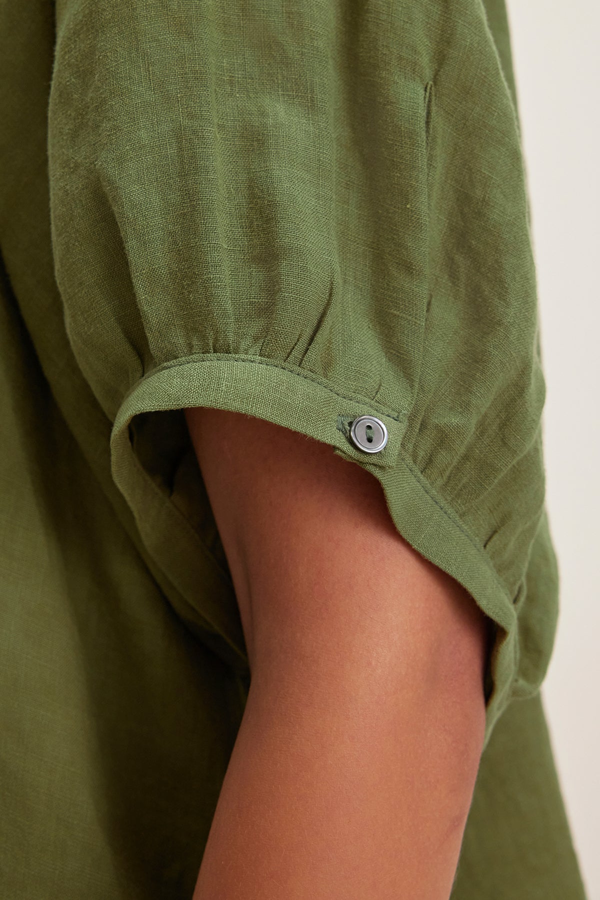   Close-up of the JAIMI LINEN TOP by Velvet by Graham & Spencer, a green short-sleeve shirt crafted from lightweight woven linen with a button tab detail on the sleeve. 