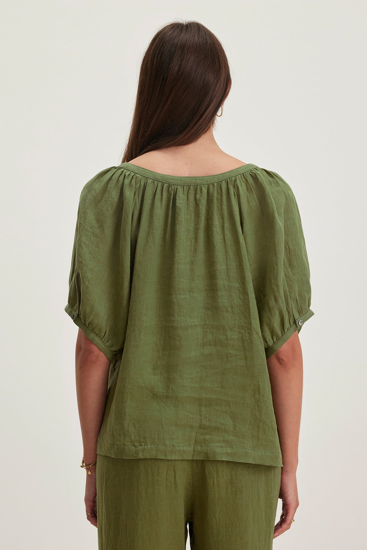   The woman is seen from the back, wearing a JAIMI LINEN TOP by Velvet by Graham & Spencer; it's a green, loose-fitting blouse made of lightweight woven linen featuring short sleeves. 