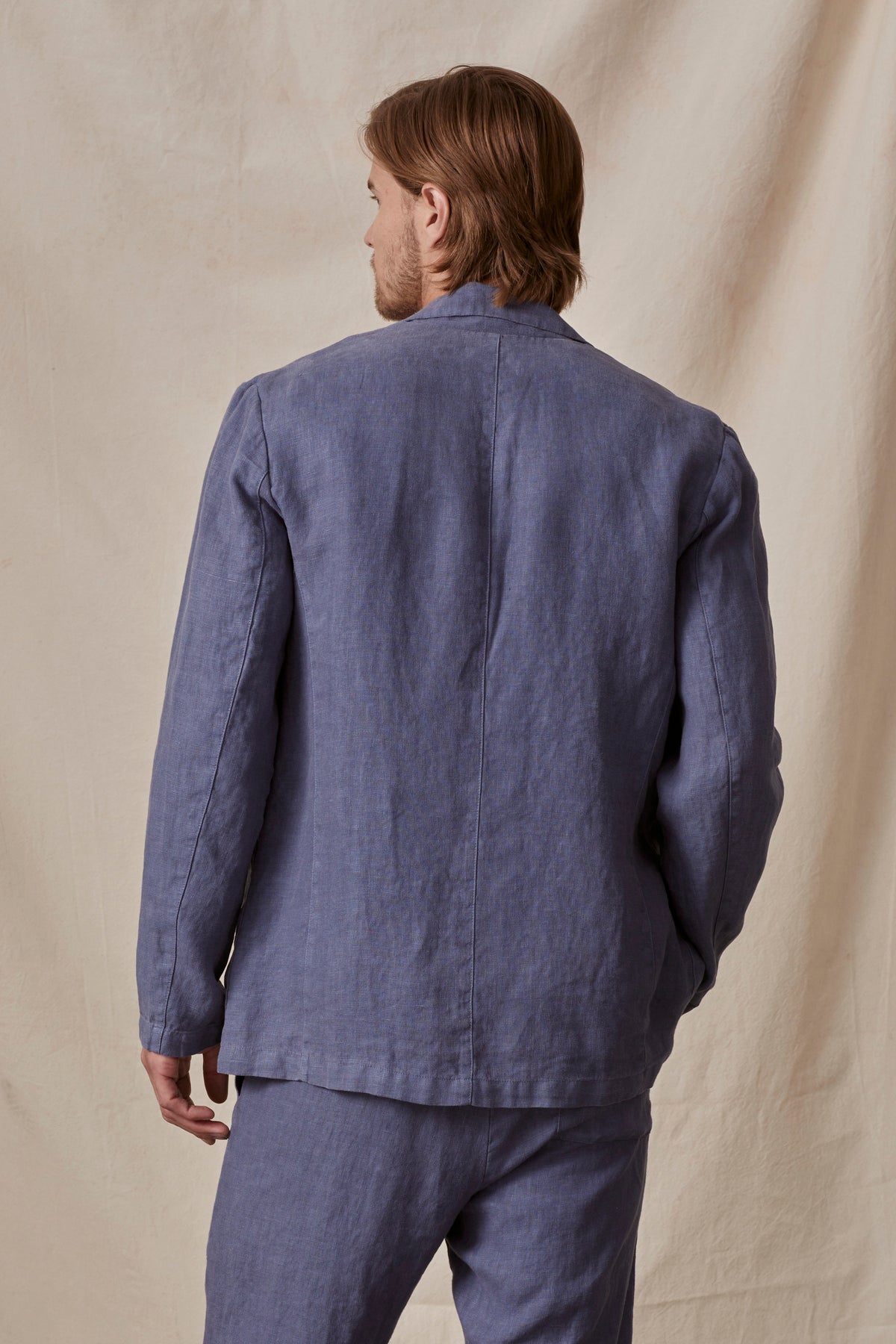   A man viewed from the back wearing a casual blue linen shirt and Phelan Linen Pant against a beige background in the JOSHUA LINEN BLAZER by Velvet by Graham & Spencer. 