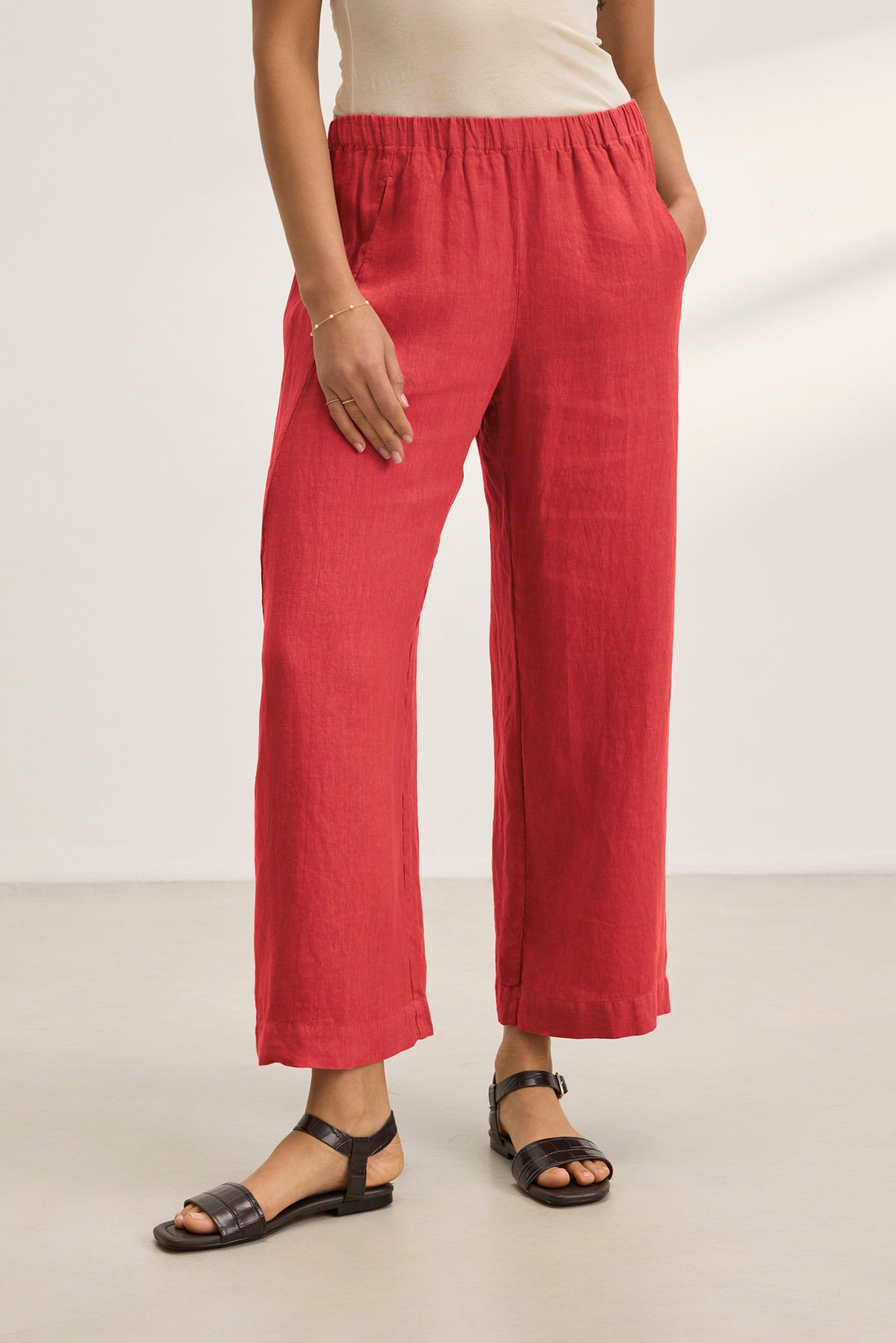   A person is indoors on a light floor, wearing Velvet by Graham & Spencer's stylish LOLA LINEN PANT in red with an elastic waist and paired with black sandals. Only the lower body is visible. 