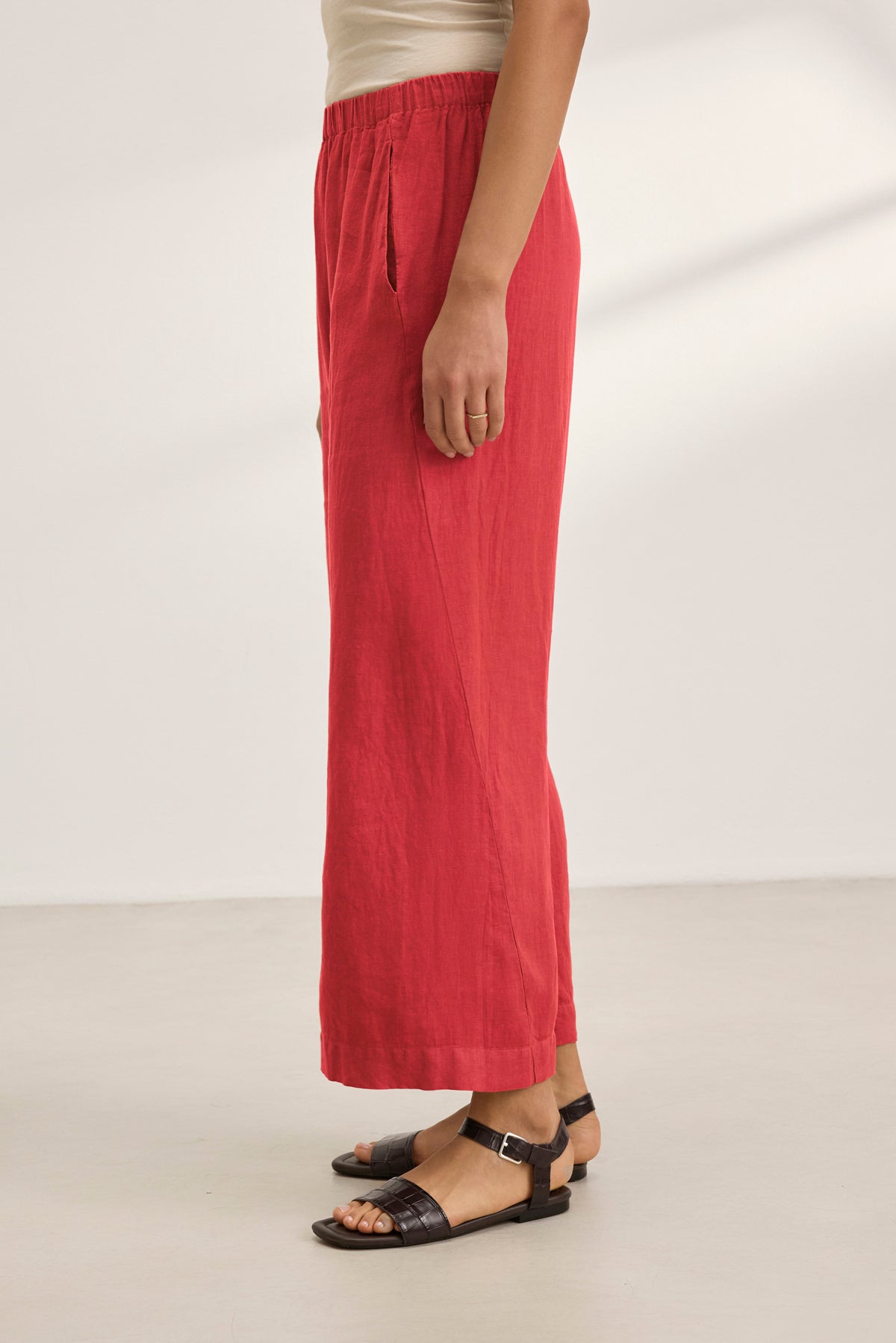   A person wearing red LOLA LINEN PANT by Velvet by Graham & Spencer with black sandals, standing on a light-colored floor. 