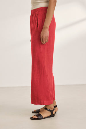 A person wearing red LOLA LINEN PANT by Velvet by Graham & Spencer with black sandals, standing on a light-colored floor.