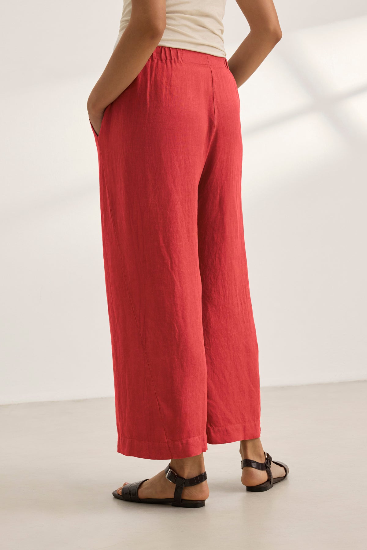   A person stands against a plain background wearing LOLA LINEN PANT from Velvet by Graham & Spencer in red, featuring an elastic waist, paired with black sandals. 