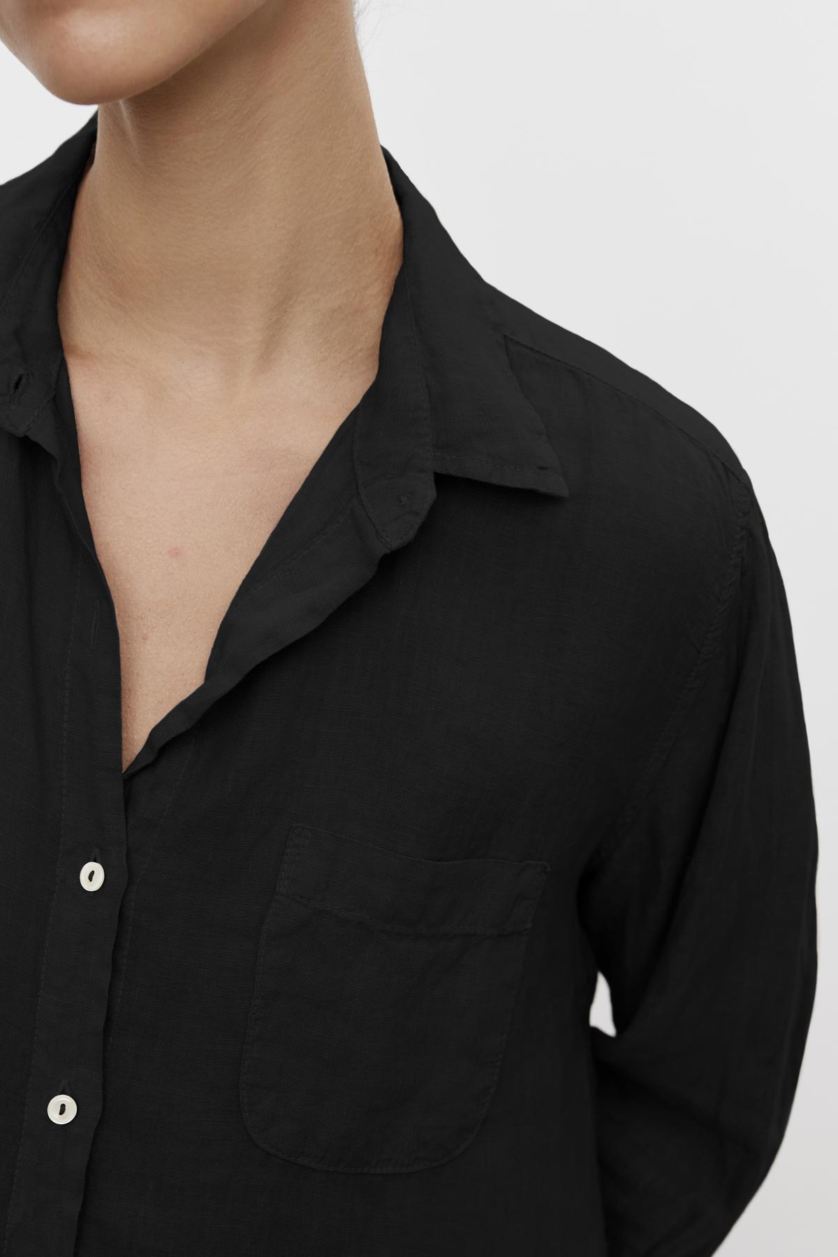   Close-up of a person wearing a Velvet by Jenny Graham MULHOLLAND LINEN SHIRT with a front pocket and an open collar. The shirt's fabric appears lightweight and textured, featuring a relaxed silhouette. The background is plain and light-colored. 