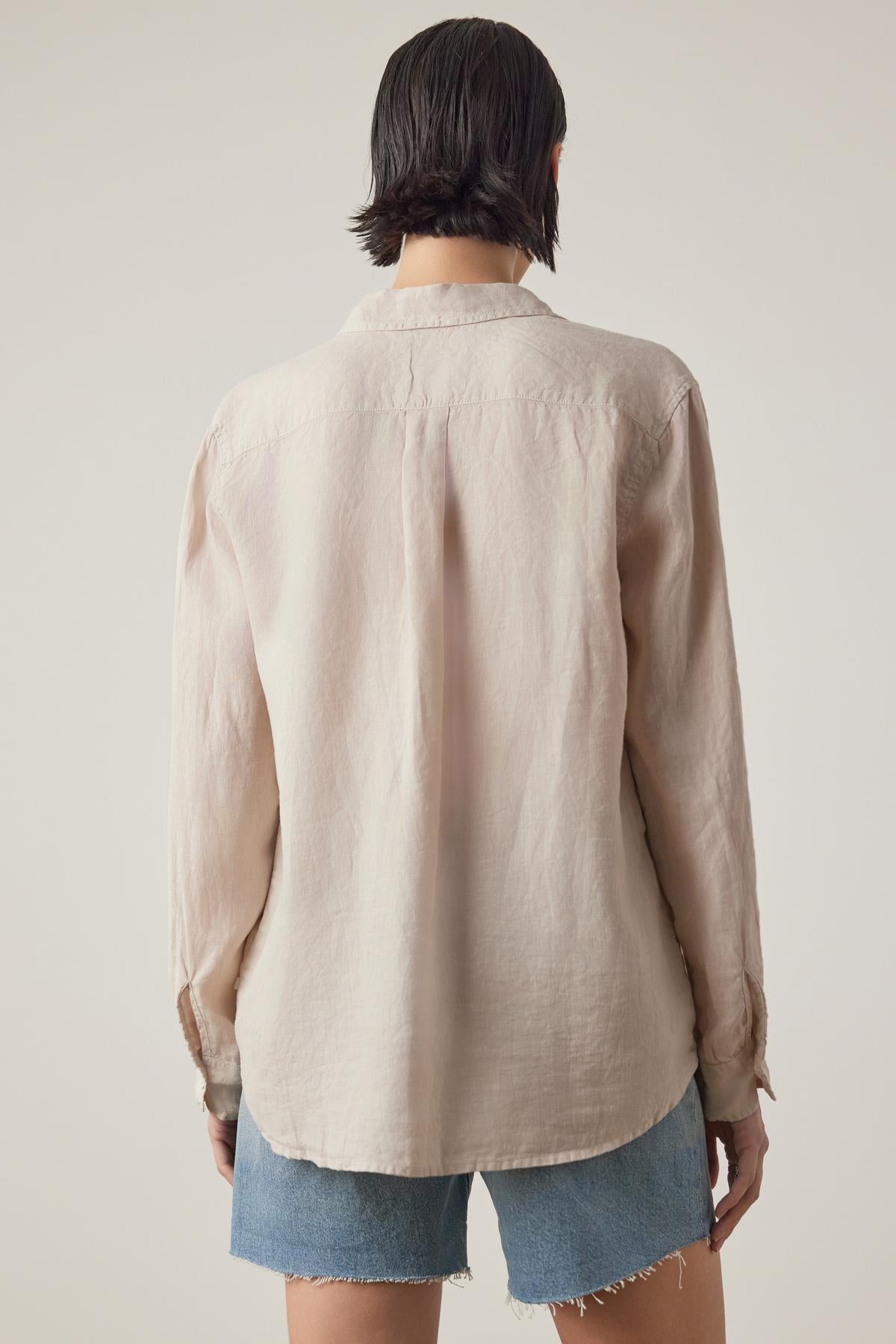   Person with short dark hair wearing a relaxed silhouette MULHOLLAND LINEN SHIRT by Velvet by Jenny Graham and cut-off denim shorts, facing away from the camera. 