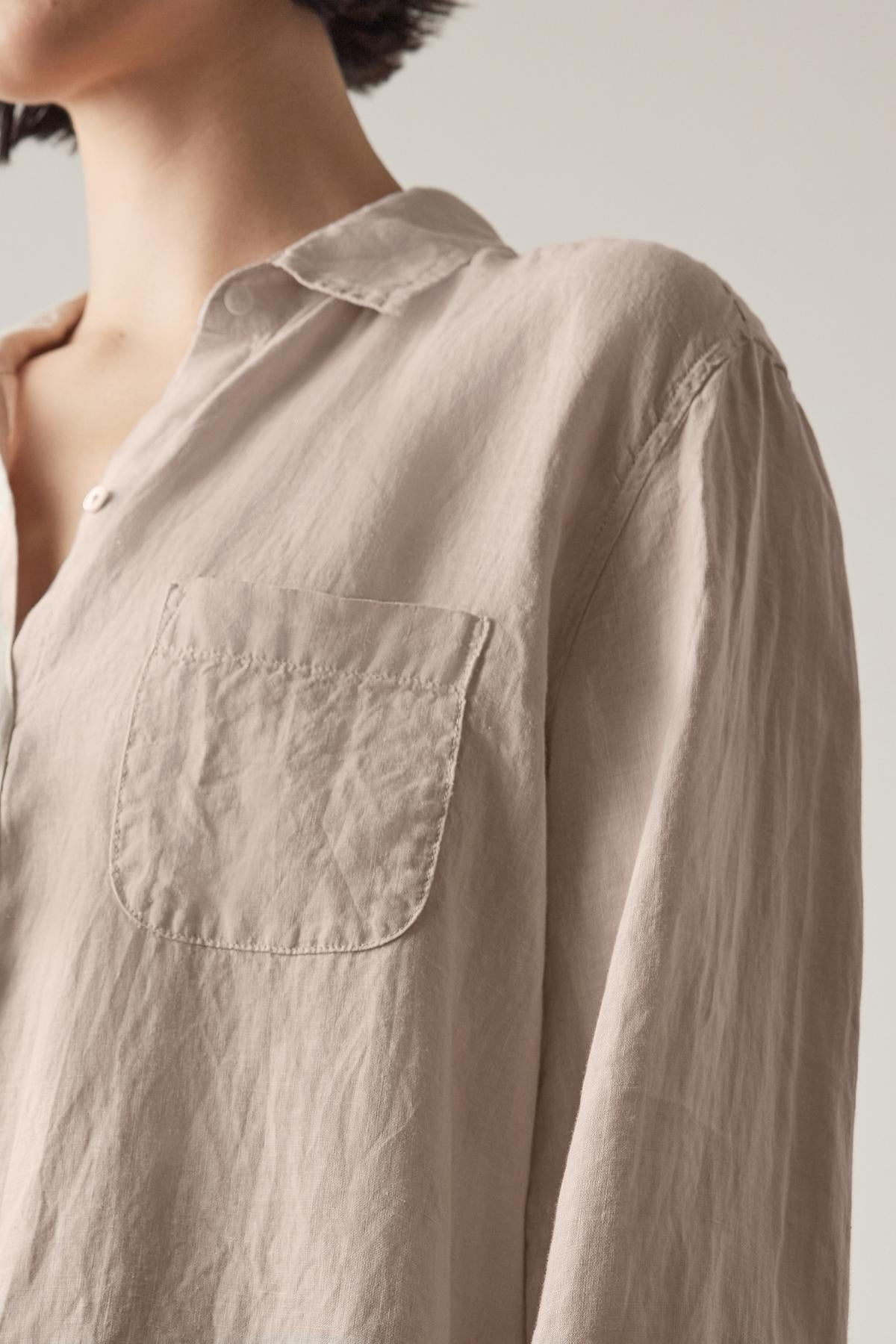 Close-up of a person wearing a light-colored, rumpled MULHOLLAND LINEN SHIRT by Velvet by Jenny Graham with a front pocket, showcasing the relaxed silhouette of the upper torso and partial neck.-36890595459265