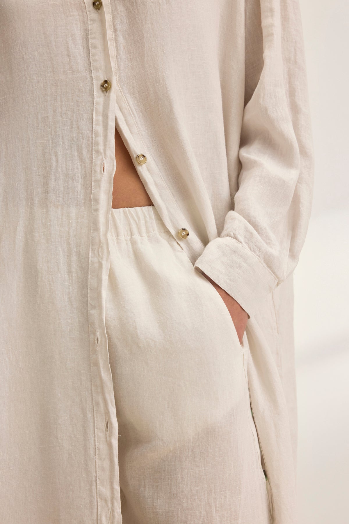   A versatile woman in the NICOLE LINEN DRESS by Velvet by Graham & Spencer exhibits effortless style, with one hand in the pocket of matching pants, epitomizing breathable comfort. 